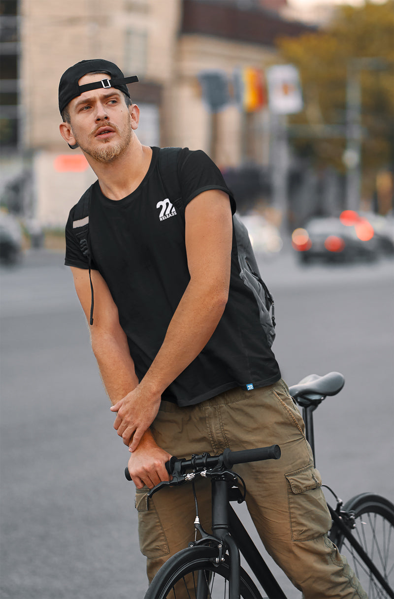 Male model wearing the Release Twenty-Two logo tee holding a mountain bike on a busy street